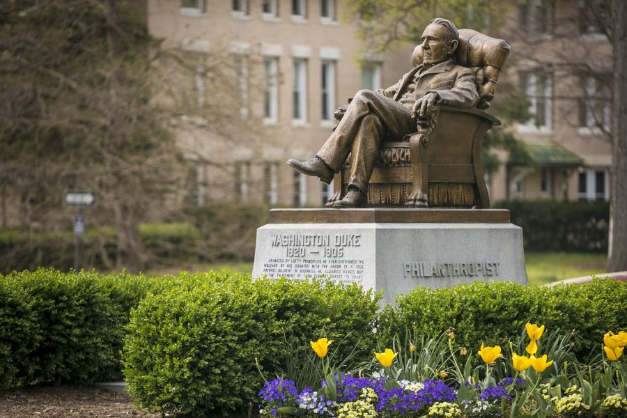 The Washington Duke statue sits amongst bushes and colorful flowers on Duke Universities campus.