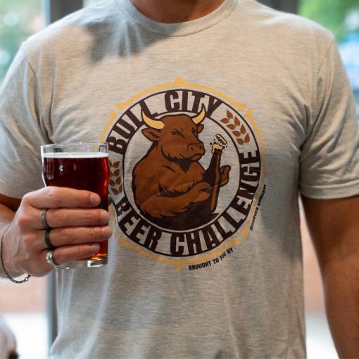 A man wearing a Bull City Beer Challenge shirt holds an amber beer.