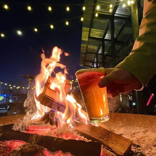 A person holds a beer by firelight at Ponysaurus Brewing Company in Durham, NC.