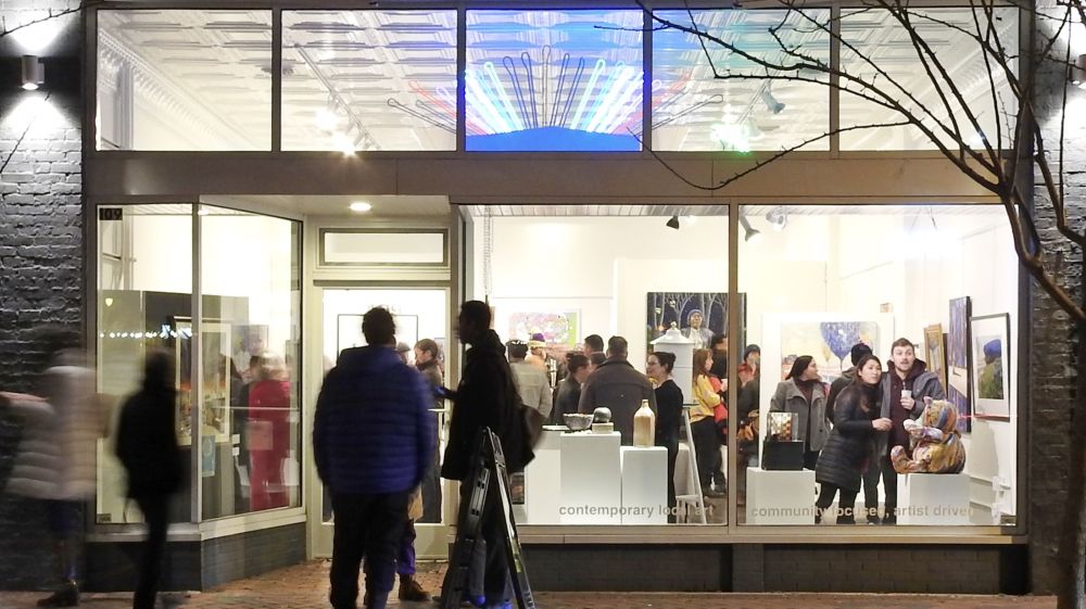 A nighttime view of a crowd inside a 5 Points Gallery from the outside.