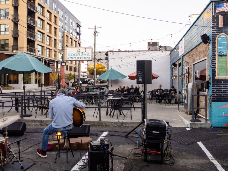A musician plays guitar in front of diners eating on the patio of Goorsha.
