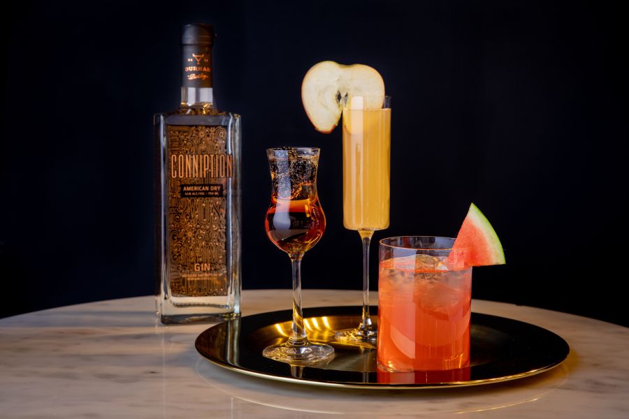 3 cocktails sit on a tray next to a bottle of Conniption Gin.