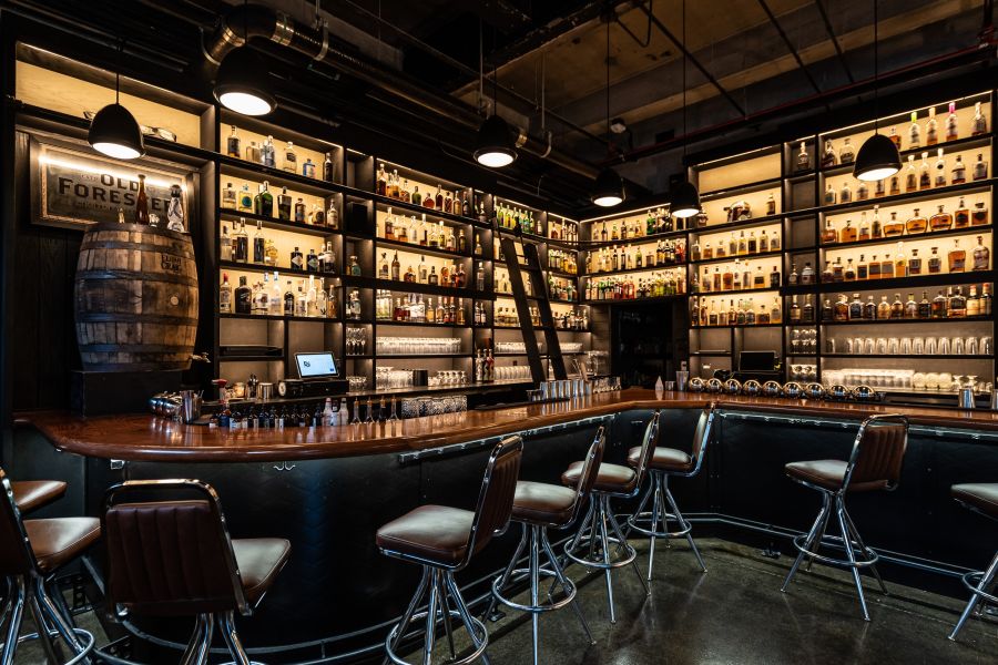 Empty stools sit waiting for guests to fill them behind the warmly lit bar of Dram and Draught in Durham, NC.