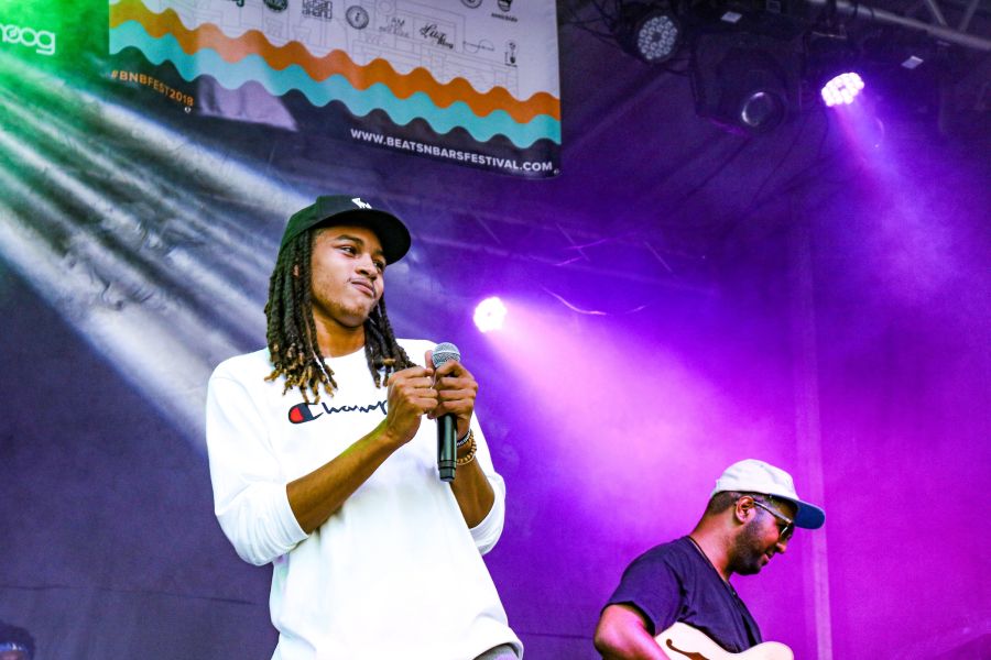 Performers onstage with purple lighting and a Beats N Bars Festival banner behind them.