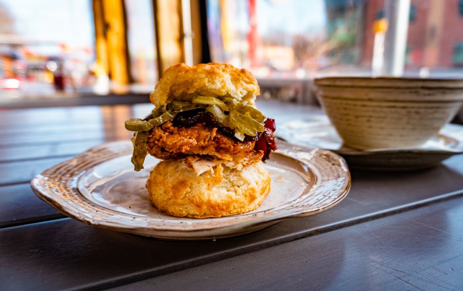 A breakfast biscuit is stacked high with fried chicken and toppings on a table at GRUB.