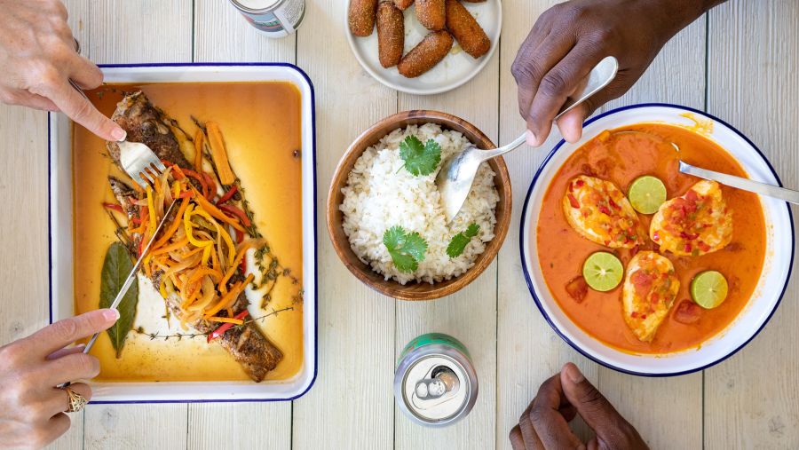 Diners dig into fish, hush puppies, and rice on a white picnic table.