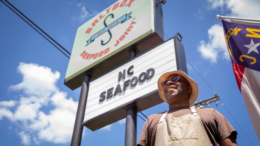 Chef Ricky Moore stands underneath the sign for his restaurant, Salt Box Seafood Joint.