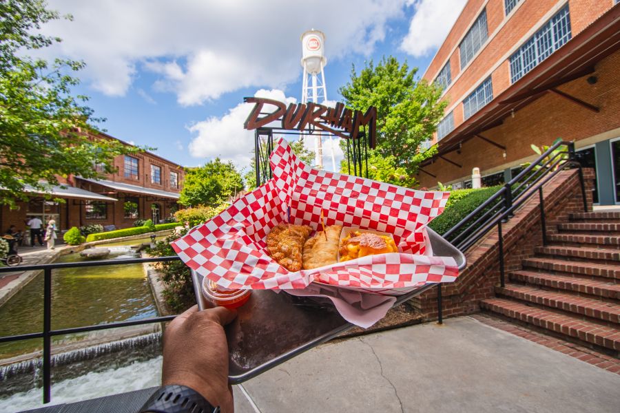 A hand holds up a tray of empanadas from Boricua Soul in front of the Durham sign.