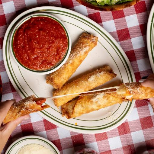 hands pull apart a fried mozzarella stick above a plate of sticks and marinara sauce, with a salad and chicken parm on plates