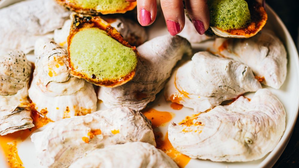 A hand reaches for an oyster on a colorful plate from Nana's