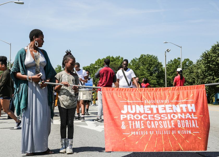 A group of people carries an orange banner that says Juneteenth Processional time capsule.