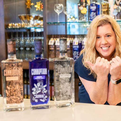Melissa Katrincic makes bull horns and poses with her award-winning Conniption Gin behind the bar at Durham Distillery.