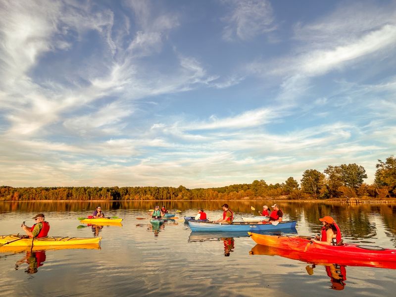 Seven kayaks on the water at Falls Lake with a backdrop of fall trees.