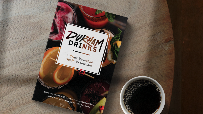 A booklet called Durham Drinks: A Craft Beverage Guide to Durham sits on a table next to a cup of coffee.